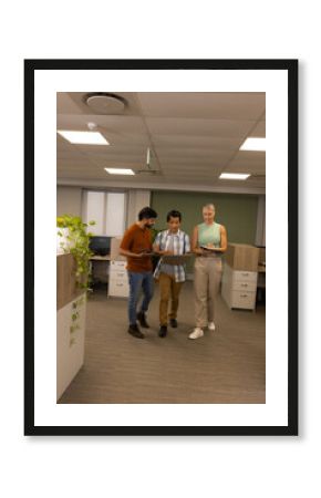 Walking diverse colleagues reviewing documents in open-plan office, with tablet laptop and notebook