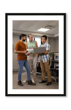 Collaborating Diverse coworkers reviewing documents in office space, with silver laptop and pen