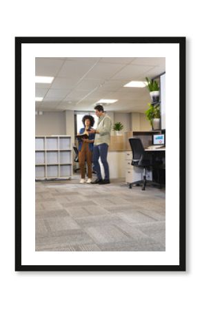 Diverse coworkers reviewing notes and charts in open-plan office, with tablet and monitor