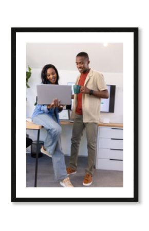 Collaborating African American colleagues checking laptop at office, with coffee mug and monitors