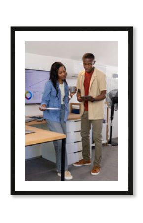 African American coworkers analyzing data on monitor in office, with report and tablet