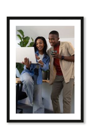 Collaborating African American colleagues discussing silver laptop at desk in office with teal mug