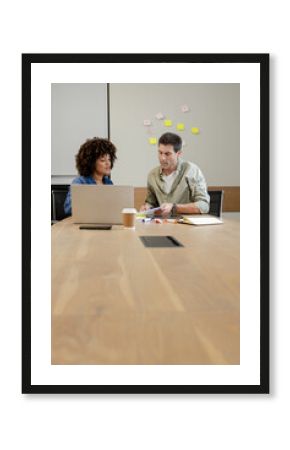 Collaborating diverse colleagues reviewing documents in modern office, with laptop and sticky notes