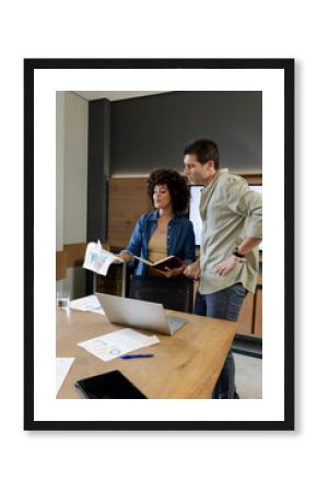 Diverse colleagues reviewing printed charts in office meeting room, with silver laptop and notebook