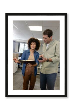 Diverse coworkers collaborating on project details in modern office, with notebook, smartphone