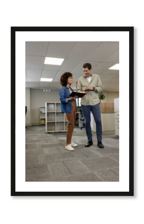 Discussing Diverse coworkers standing in modern open-plan office, using notebook and eyeglasses
