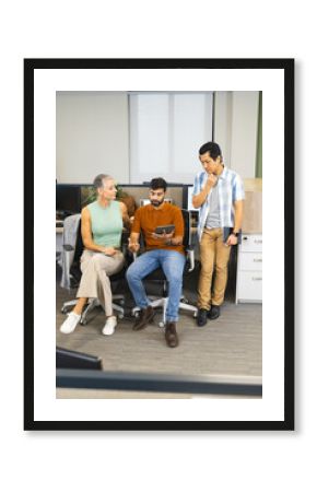 Diverse coworkers discussing ideas at desk divider in modern office, with tablet, smartphone