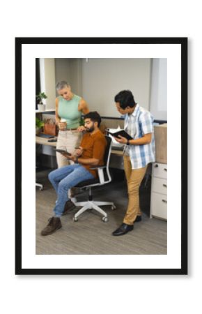 Diverse coworkers discussing project around desk in office, with tablet and notebook