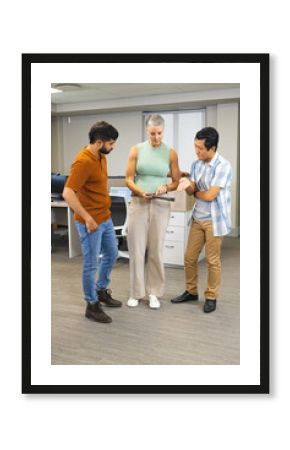 Diverse coworkers reviewing data on tablet in modern open-plan office, with computer monitors