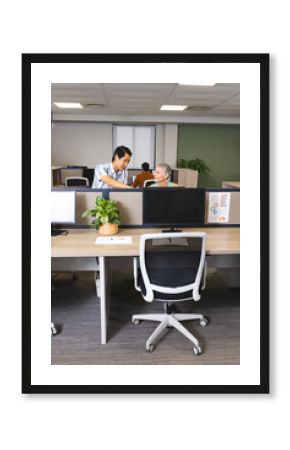 Discussing work Diverse coworkers leaning over cubicle wall in modern office, with monitors