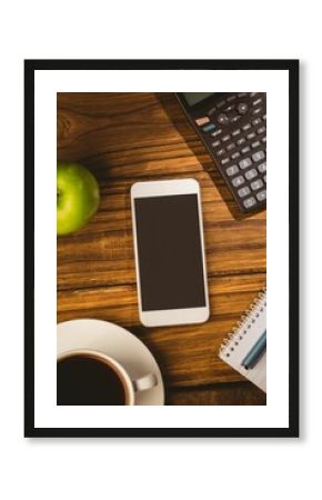 Showing desk with white smartphone alongside calculator, green apple, coffee, notebook and blue pen