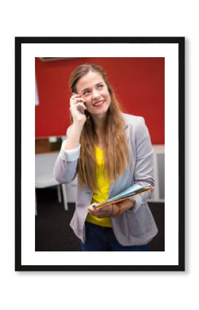 Female worker wearing gray blazer holding smartphone, folder, standing in red accent wall office