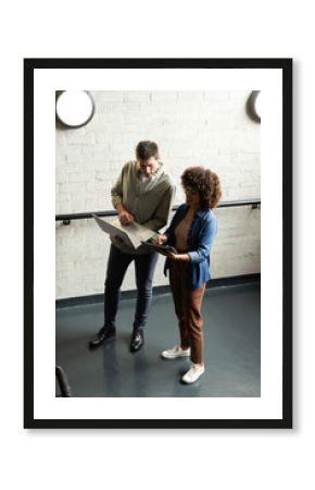 Diverse colleagues reviewing content in industrial office corridor, with tablet, stylus and laptop