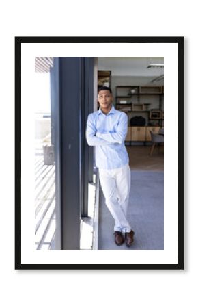 Confident businessman in blue shirt standing by office window, looking thoughtful