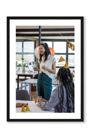 Asian woman holding glass, smiling during office celebration with colleagues