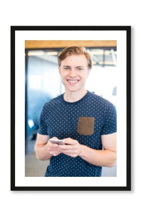 Man standing holding smartphone at waist level in office with glass partitions, copy space