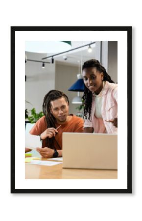 African American colleagues leaning and pointing at laptop while reviewing papers in modern office