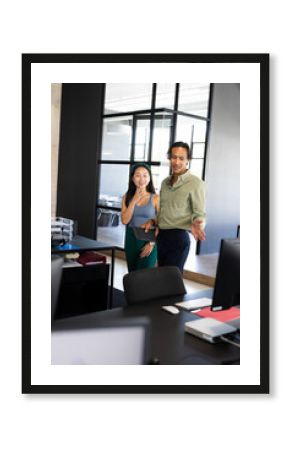 Diverse colleagues discussing project while standing in modern office, smiling and engaged