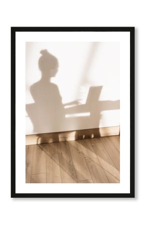  shadow on the wall of a woman sitting and working on her laptop