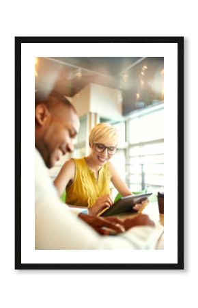 Two creative millenial small business owners working on social media strategy using a digital tablet while sitting at desk