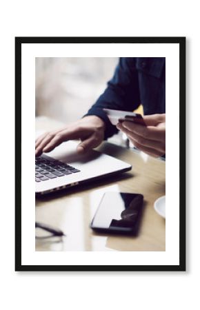 Businessman holding plastic credit card in hand and using laptop computer while sitting at the wooden table.Man making online shopping.Blurred background.Vertical.
