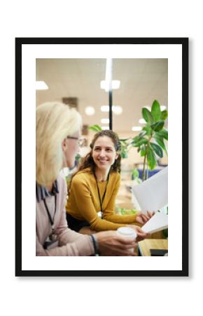 Two contemporary businesswomen in smart casual sitting in office and discussing financial questions