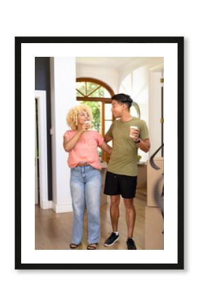 Young diverse couple enjoying coffee break while unpacking boxes in new home
