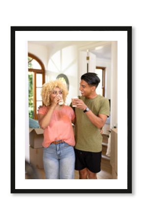 Young diverse couple enjoying coffee break while unpacking boxes in new home