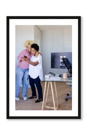 Friends hugging and laughing while looking at smartphone in modern office