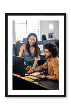 Colleagues collaborating at office desk, discussing project on computer screen