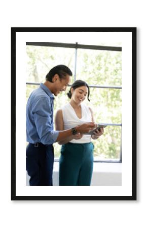 Asian colleagues discussing project on tablet in bright office, smiling and engaged