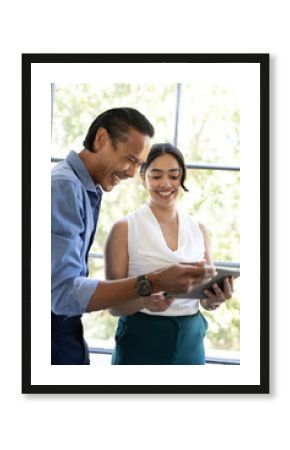 Colleagues collaborating with tablet, smiling and discussing ideas in bright office