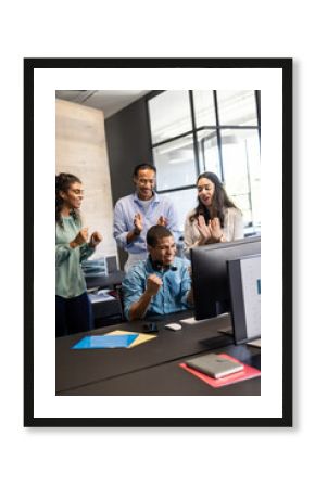 Team celebrating success at office, smiling and clapping around computer screen