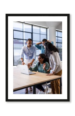 Celebrating success, diverse business team collaborating on laptop in modern office