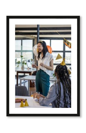 Asian woman holding glass, smiling during office celebration with colleagues