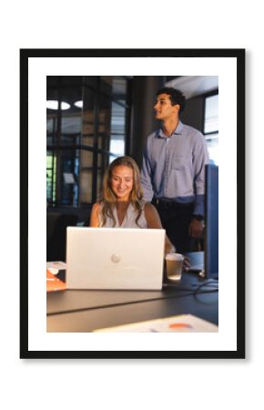 Smiling colleagues collaborating on laptop in modern office during evening work