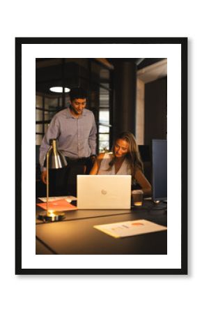 Colleagues collaborating on laptop in modern office during late-night work session