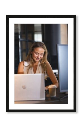 Businesswoman working late at office, smiling while using laptop with coffee nearby