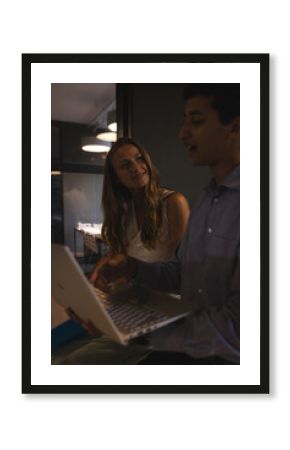Colleagues discussing project while using laptop in modern office at night
