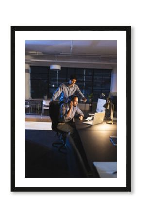 Businessmen working late in office, discussing project on laptop with focus