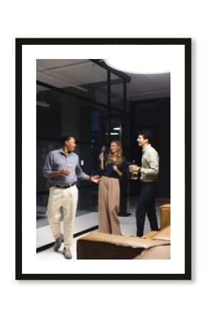 Colleagues enjoying drinks and laughing together during night office gathering