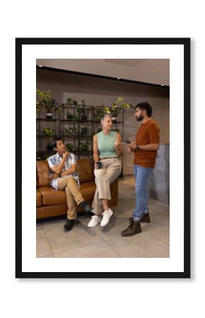Talking diverse colleagues sitting in modern office lounge, with coffee mugs and smartphone