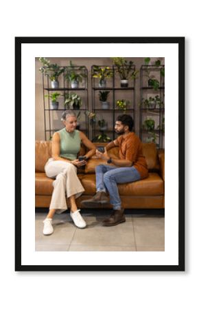 Chatting Diverse coworkers sipping coffee from mug on leather sofa at office lounge, amid plants