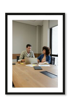 Diverse colleagues reviewing charts on conference table in office, with laptop and coffee cup