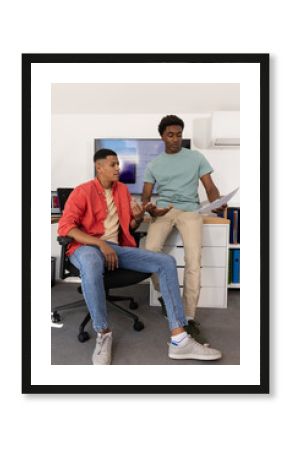Discussing diverse male colleagues looking at document in modern office, with widescreen monitor