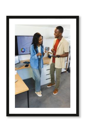 Discussing African American colleagues standing at desk in office, with laptop and chart on monitor