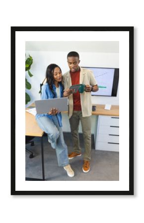 Collaborating African American colleagues discussing data on monitor at office desk, with laptop