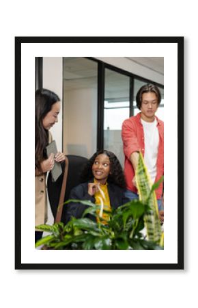 Diverse colleagues collaborating around desk in office interior, using tablet beside potted plants