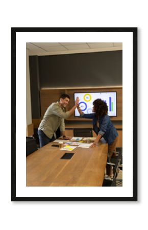 High-fiving Diverse colleagues celebrating success around conference table, with coffee and charts