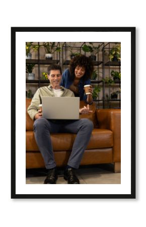 Collaborating Diverse coworkers using laptop and coffee cups in office lounge, with leather sofa